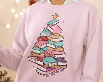 Pode incluir: Uma camisa de frio rosa com um gráfico de uma árvore de Natal feita de livros empilhados. O texto "Oh Christmas Tree" está impresso abaixo do gráfico.