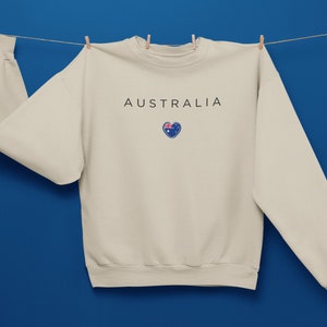 May include: A beige sweatshirt with the word "AUSTRALIA" printed on the front, and a small heart with the Australian flag inside.