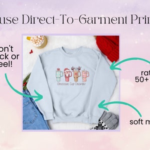 Op de afbeelding: Een lichtblauw sweatshirt met een kerstthema ontwerp met een rij bekers met gezichten en de tekst "Obsessive Cup Disorder". Het sweatshirt is gemaakt van een zacht materiaal en is geschikt voor 50+ wasbeurten.