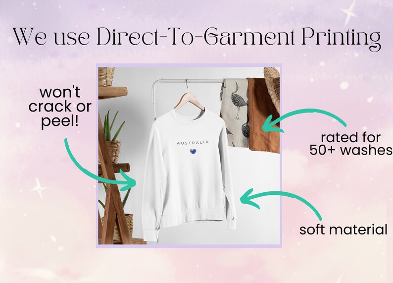 May include: White sweatshirt with the word "AUSTRALIA" and a heart with the Australian flag printed on it. The sweatshirt is hanging on a wooden rack. Text on the image reads "We use Direct-To-Garment Printing", "won't crack or peel!", "rated for 50+ washes", and "soft material".