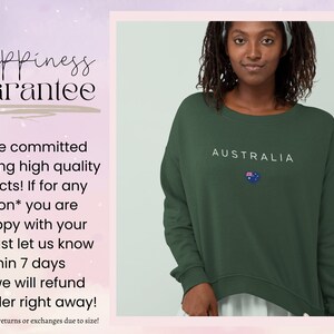 May include: A green sweatshirt with the word "AUSTRALIA" and a small Australian flag printed on the front. The text "Happiness Guarantee" is visible in the background.