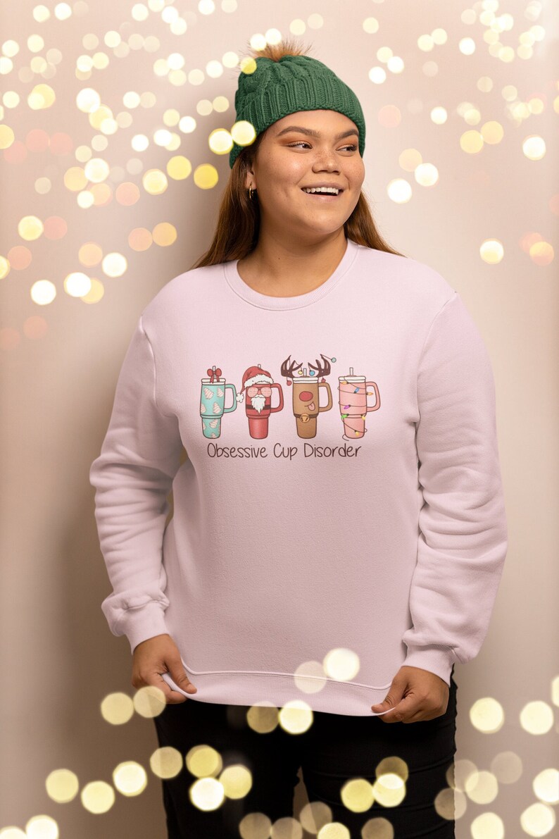 Op de afbeelding: Een roze sweatshirt met een afbeelding van vier kerstthemabekers met de tekst "Obsessive Cup Disorder".