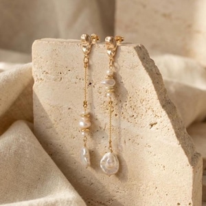 May include: A pair of gold-tone drop earrings featuring irregular, organic-shaped white pearls suspended from delicate gold chains. Each earring has a textured gold stud top and multiple pearl accents of varying sizes arranged along the length.