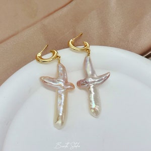 May include: A pair of gold hoop earrings with a pearl cross pendant. The pearls are a light pink and white color.
