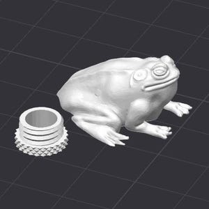 Op de afbeelding: Een witte, 3D-geprinte kikkerfiguur met gedetailleerde kenmerken, naast een bijpassende cilindrische component. De kikker zit met gesloten ogen. De component heeft een getextureerde, decoratieve basis.