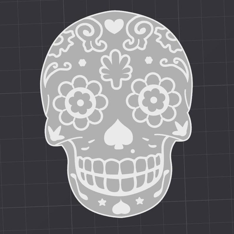 May include: A white sugar skull with intricate floral designs, a heart, and a spade symbol. The skull has a toothy grin and is decorated with small stars.
