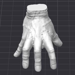 Puede incluir: Una mano blanca estilizada con costuras visibles a lo largo de las costuras. La mano está posada con los dedos ligeramente separados, y la zona de la muñeca también está cosida. El diseño sugiere un personaje o accesorio de un tema de terror o fantasía.
