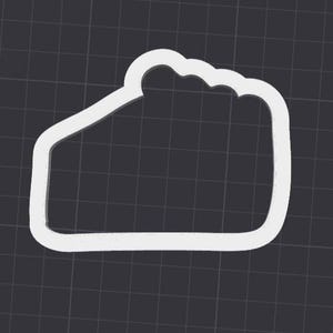 Könnte beinhalten: Ein weißer Ausstecher in Form eines Kuchenstücks. Der obere Rand hat ein gewelltes Design. Der Ausstecher befindet sich vor einem dunkelgrauen Gitterhintergrund. Der Ausstecher besteht aus einem weißen Material.