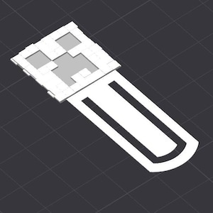 May include: White plastic bookmark featuring a Minecraft Creeper face design. The bookmark is long and thin with a curved end.