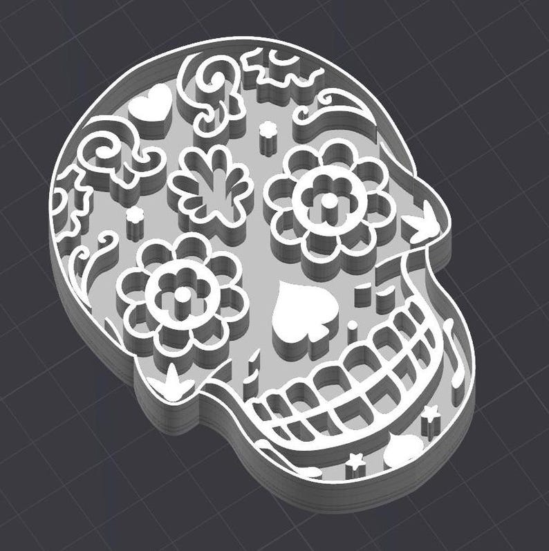 May include: White sugar skull with intricate floral and heart designs. The skull is a traditional symbol of Day of the Dead.