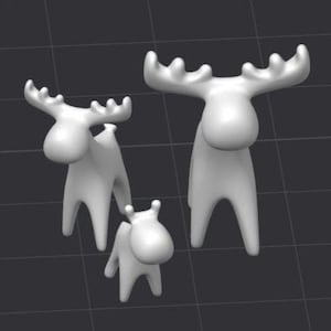 Könnte beinhalten: Drei weiße Elchfiguren in verschiedenen Größen. Die Elche haben stilisierte Körper und große Geweihe. Die Figuren sind auf einer dunkelgrauen Oberfläche angeordnet.