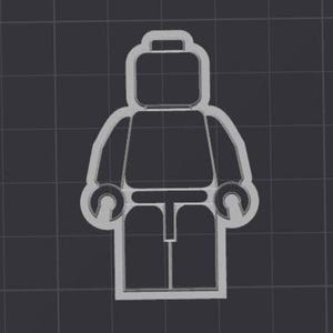May include: A gray plastic cookie cutter in the shape of a classic toy figure. The cutter has a rectangular head, a torso, arms with circular hands, and legs. The background is a dark gray grid.