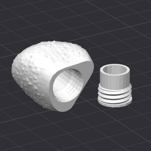 Op de afbeelding: Een 3D-geproduceerde, gebroken witte flesstopper met een getextureerde, afgeronde bovenkant en een grote, cirkelvormige opening. Daarnaast een cilindrisch stuk met horizontale ribbels. De objecten staan tegen een donkere rasterachtergrond.
