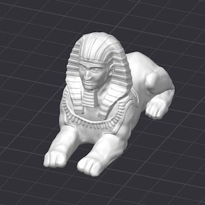 Puede incluir: Escultura de cerámica blanca de una esfinge con cabeza humana y cuerpo de león. La esfinge lleva un tocado con un patrón decorativo.
