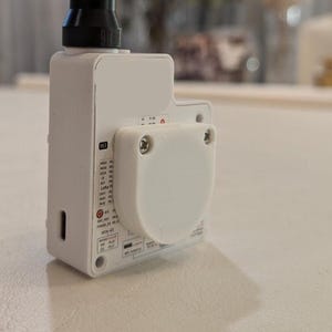 May include: A white electronic device with a black antenna and a white, rounded cover secured by screws. The device has various ports and labels, including "M3" and "Wire-SC". The background is a blurred, neutral color.