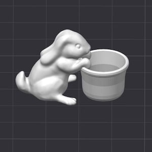 May include: A white ceramic rabbit figurine is reaching its paw into a white ceramic bucket. The rabbit has a long, floppy ear and a short, stubby tail.