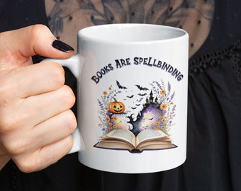 May include: White ceramic mug with a Halloween-themed design. The mug features an open book with a spooky castle and bats flying above it. The text "Books Are Spellbinding" is printed on the mug.