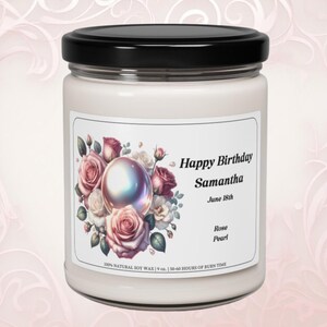 May include: A white candle in a glass jar with a black lid. The label features a floral design with pink roses and a pearl. Text on the label reads "Happy Birthday Samantha June 18th". The candle is 9 oz.
