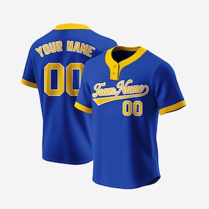May include: A royal blue baseball jersey with gold trim and lettering. The front of the jersey has the text "Team Name" in a gold cursive font with the number "00" below it. The back of the jersey has the text "YOUR NAME" in gold with the number "00" below it.