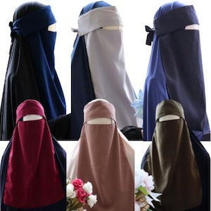May include: A selection of niqabs in diverse colours: black, navy, burgundy, and olive green. Each garment includes a head covering and face veil, some with a band across the forehead. The materials appear smooth and opaque.