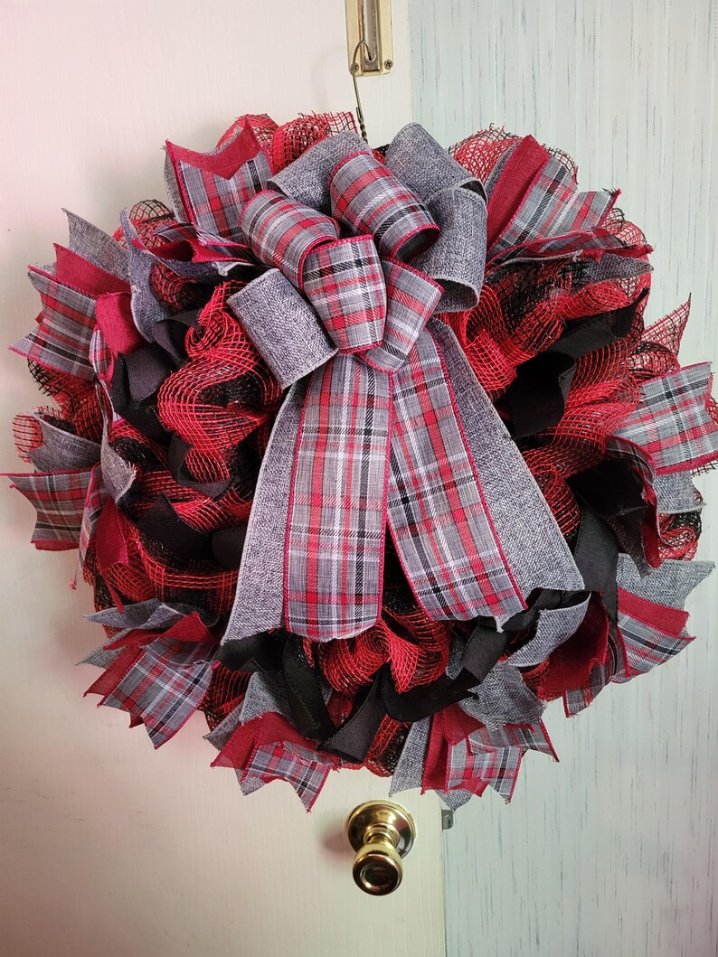 May include: A red, black, and gray plaid wreath with a large bow. The wreath is made of mesh and has a rustic look.