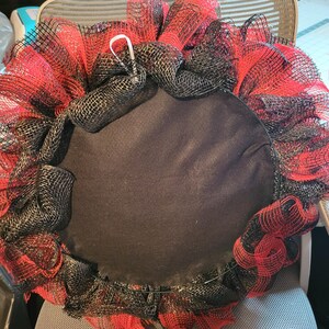 May include: A black and red wreath with a black felt backing. The wreath is made of mesh and has a wire frame.