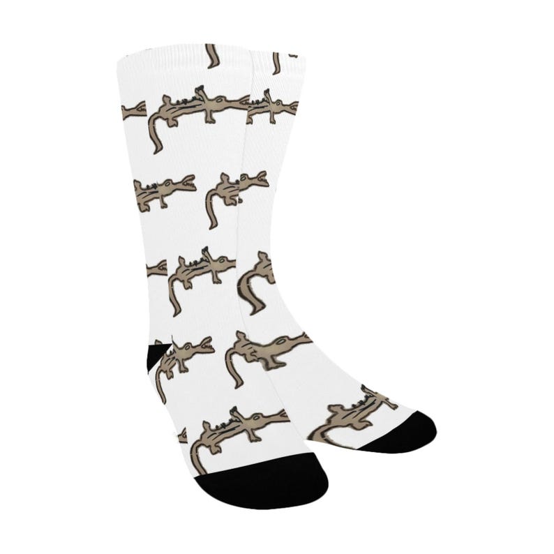 May include: A pair of white socks with a repeating pattern of brown alligators. The socks have black toe and heel.