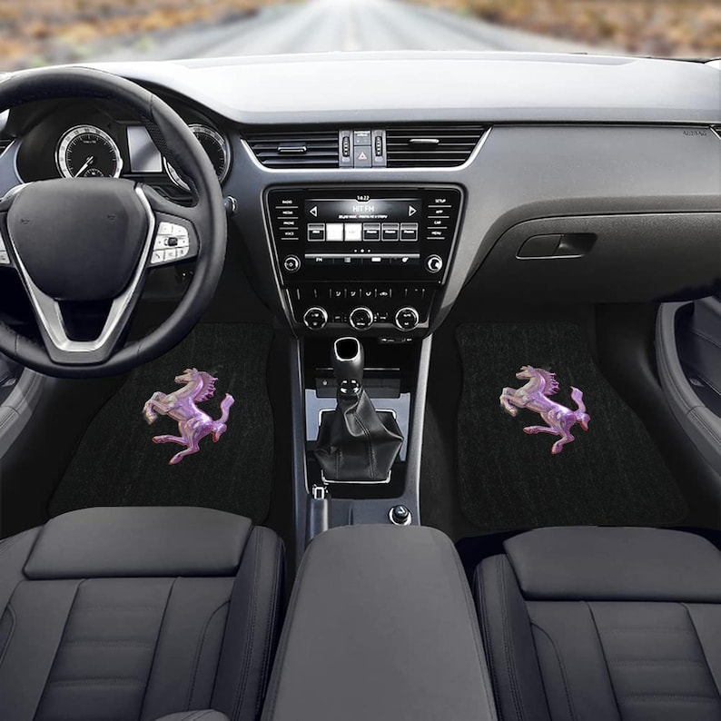 Pu&ograve; includere: Tappetini neri per auto con un'emblema di cavallo viola e bianco. I tappetini sono all'interno di un'auto con volante, cruscotto e sedili visibili. L'emblema del cavallo &egrave; su entrambi i tappetini.