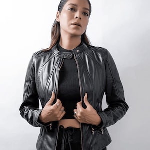 Peut inclure: Une femme portant une veste en cuir noire avec une fermeture &eacute;clair. Elle porte un haut noir et un pantalon noir.