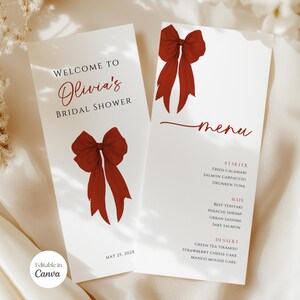 Op de afbeelding: Twee witte menukaarten voor een bruidsdouche met een rode strik. Op de linkerkaart staat "Welkom bij Olivia's Bridal Shower" en op de rechterkaart staat "menu". Het menu bevat voorgerechten, hoofdgerechten en desserts.