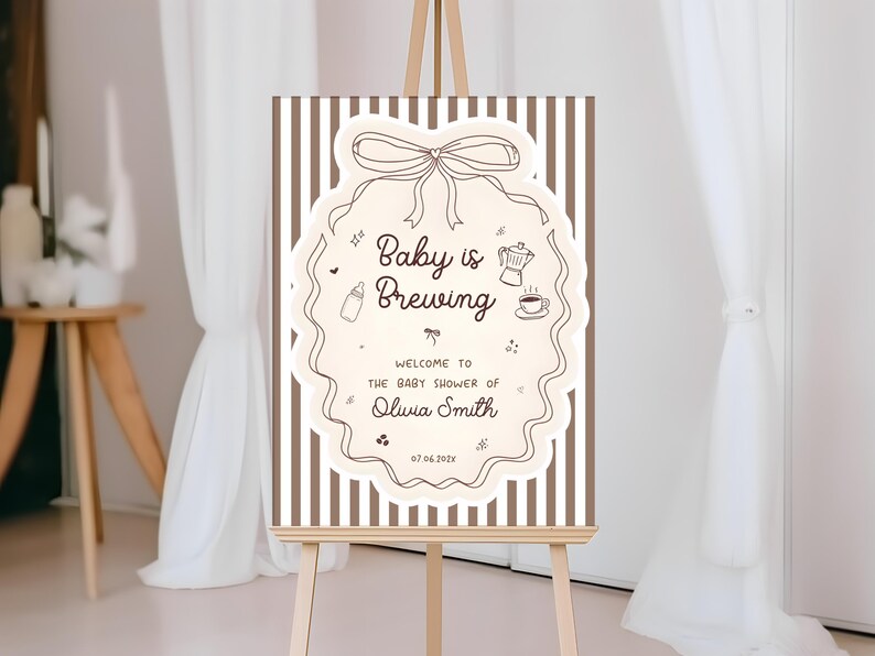 K&ouml;nnte beinhalten: Willkommensschild f&uuml;r eine Babyparty auf einer Staffelei. Das Schild zeigt die Worte "Baby is Brewing" in einem dekorativen Rahmen. Das Schild enth&auml;lt auch den Namen Olivia Smith und das Datum 07.06.202x. Der Hintergrund hat vertikale braune und wei&szlig;e Streifen.