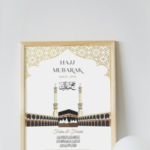 Puede incluir: Una impresi&oacute;n enmarcada con un marco de madera clara. La impresi&oacute;n presenta el texto "HAJJ MUBARAK" y caligraf&iacute;a &aacute;rabe, junto con una ilustraci&oacute;n de la Kaaba y los minaretes. La impresi&oacute;n est&aacute; sobre un fondo blanco.