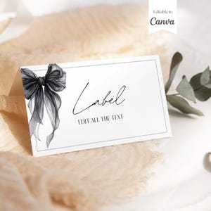 以下が含まれることがあります： 黒いリボンイラストと、筆記体で「Label」と書かれた白いカード。下には「EDIT ALL THE TEXT」という文字。右上には「Editable in Canva」という文字があります。