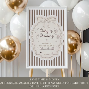 K&ouml;nnte beinhalten: Ein gerahmtes Schild f&uuml;r eine Babyparty mit dem Text "Baby is Brewing" und dem Namen "Olivia Smith". Das Schild steht auf einer Staffelei, umgeben von wei&szlig;en und goldenen Luftballons. Das Schild hat eine Schleife, eine Flasche, eine Kaffeekanne und eine Tasse Kaffee.