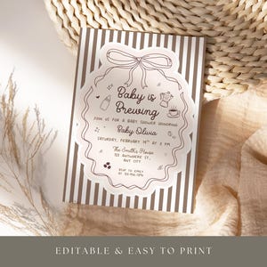 May include: A baby shower invitation with a brown and white striped background. The invitation features a decorative border with the text "Baby is Brewing" and event details. The invitation is surrounded by a neutral-toned background.