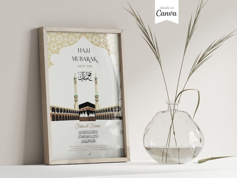Puede incluir: Una impresi&oacute;n enmarcada con las palabras "Hajj Mubarak" y caligraf&iacute;a &aacute;rabe, que presenta una ilustraci&oacute;n de la Kaaba en La Meca. La impresi&oacute;n tiene un dise&ntilde;o geom&eacute;trico dorado en la parte superior y est&aacute; en un marco de madera clara. Un jarr&oacute;n de vidrio transparente con tallos verdes altos y delgados est&aacute; en primer plano.
