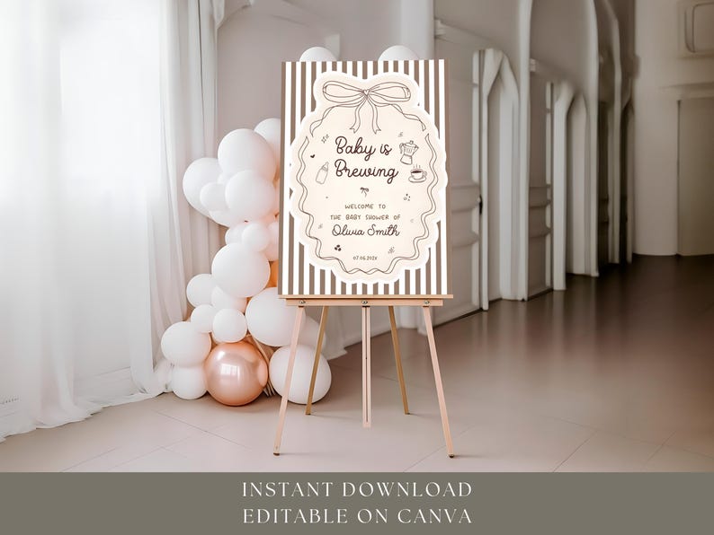 K&ouml;nnte beinhalten: Ein Willkommensschild f&uuml;r eine Babyparty mit dem Text "Baby is Brewing" in einem dekorativen Rahmen. Das Schild steht auf einer h&ouml;lzernen Staffelei, mit Luftballons im Hintergrund. Das Schild ist hellbeige mit braunen Streifen.