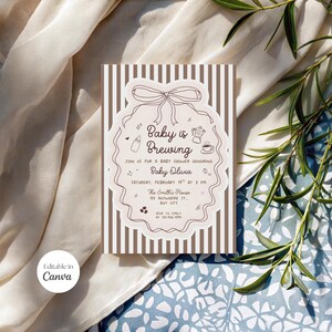 May include: Baby shower invitation with the text "Baby is Brewing" in a decorative frame. The invitation features a bow, coffee pot, and baby bottle illustrations. The background has vertical brown stripes.
