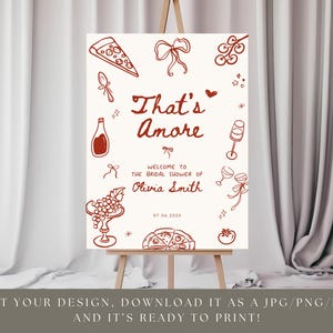 May include: A sign on an easel with the words "That's Amore" in red script, with illustrations of pizza, wine, and grapes. The sign welcomes guests to Olivia Smith's bridal shower on 07.04.2028. The sign is ready to print.