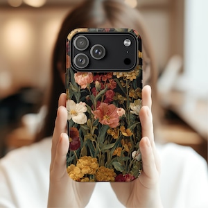 May include: A floral phone case featuring a dark background with a pattern of colorful flowers in shades of pink, yellow, and white. The case has a black camera module with three lenses and a flash.