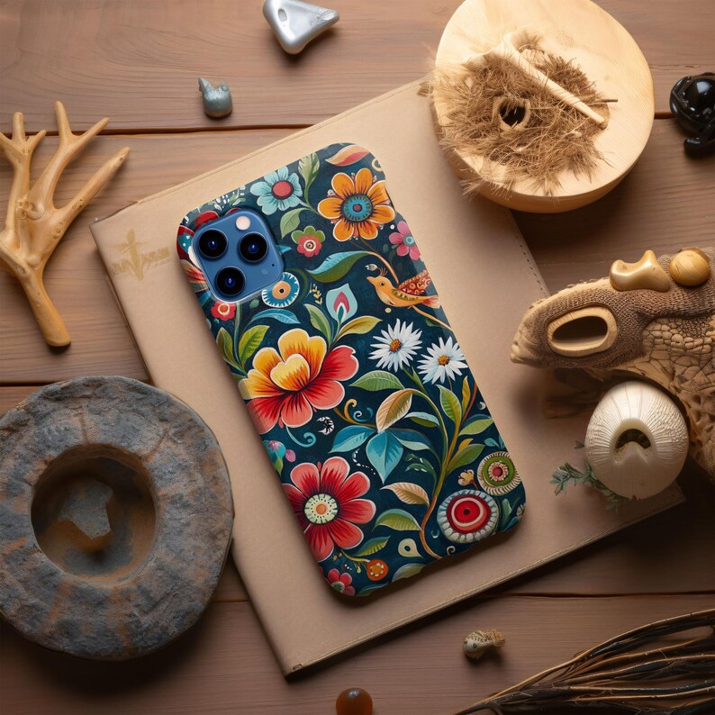May include: A phone case with a colorful floral design. The case features a dark blue background with bright red, yellow, and green flowers. A small bird is perched on a branch in the upper right corner of the case.
