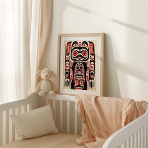 May include: A framed print of a black, red, and white Northwest Coast Indigenous art design. The design features a stylized human figure with geometric patterns.