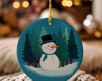May include: A round Christmas ornament with a snowman design. The ornament features a snowman with a black top hat, orange carrot nose, and a blue scarf, set against a backdrop of pine trees and snow. A gold string is attached for hanging.