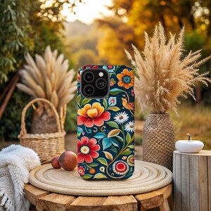 May include: A phone case with a colorful floral pattern. The case features a variety of flowers, leaves, and a small bird. The background is a dark blue.