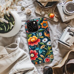 May include: A phone case with a floral design. The case is black with colorful flowers, leaves, and a bird. The camera lens is visible on the back of the case.