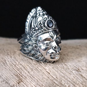 May include: A silver ring with a detailed design of a face with a black gemstone in the forehead.