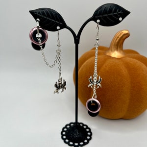 May include: A pair of dangle earrings with black and pink rings and silver spider charms hanging from silver chains.