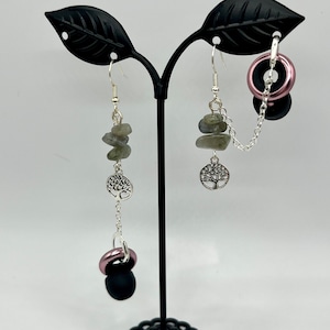 May include: A pair of silver earrings with a tree of life charm and layered green stones. One earring has a pink and black bead charm.