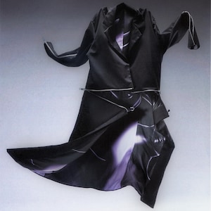 Op de afbeelding: Een zwarte satijnen jas met een blazer-stijl top en een zwierige rok. De jas heeft zilveren ritsen en een paars en wit abstract ontwerp op de rok. De mouwen zijn lang met zilveren afwerking.