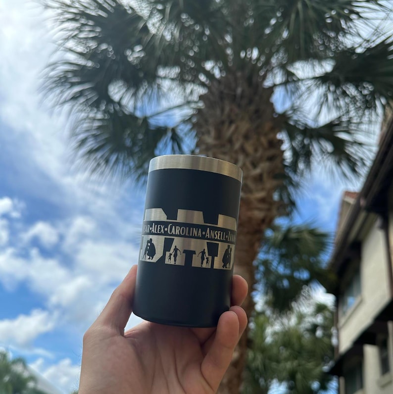 May include: Black stainless steel can cooler with a silver engraved design featuring a family of five silhouettes and the names "Alex", "Carolina", "Ansell", "Frank", and "Jay".